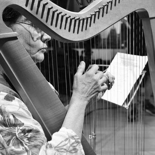 Gros plan en photo noir et blanc d'Yvonne Barth. Elle est assise derrière sa harpe, les mains sur les cordes, prête à enregistrer le son.