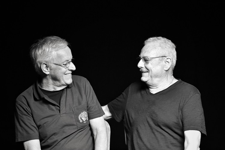Photo en noir et blanc des deux frères Peter et Kurt Bönzli. Ils sont assis face à face et rient ensemble.