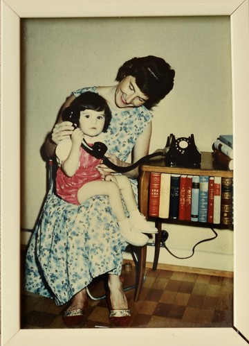 Jasmin Schweizer*, âgée d'environ 2 ans, est assise sur le dos de sa mère et tient un gros téléphone noir dans la main. Sa mère s'approche d'elle et s'éloigne. Un téléphone noir, avec des traces d'eau, se trouve sur une petite colline à côté d'elle.